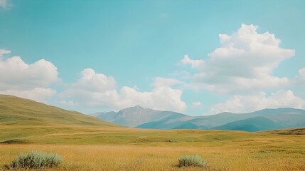 Fototapeta premium Serene mountain landscape with golden fields under a bright blue sky. Perfect for travel, nature, and peaceful mood imagery.