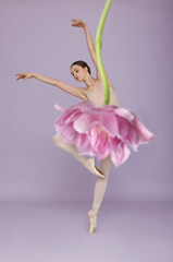 Young ballerina dancing on light violet background. Tulip flower partly covering woman as skirt