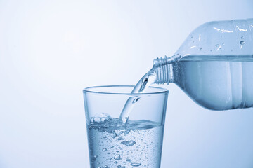 Pouring soda water from bottle into glass on light blue background, closeup. Space for text
