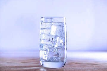 Refreshing soda water with ice cubes in glass on wooden table against light blue background, closeup