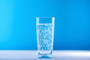 Refreshing soda water in glass on wooden table against light blue background, closeup