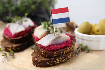 Tasty sandwiches with herring and flag of Netherlands on table