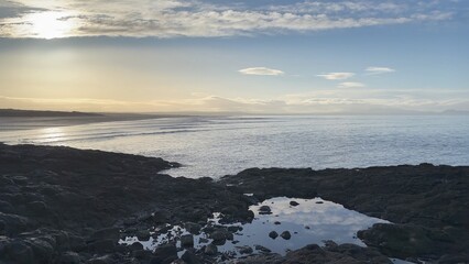 Tranquil beach reflections at Aberlady Bay in East Lothian, Scotland. Soft waves roll in under the warm glow of sunrise. Scenic views of the tranquil bay and the distant mountains - UK