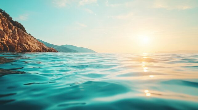 Serene view of ocean, rocky coastline, bright sun & sky. Soft focus ripples