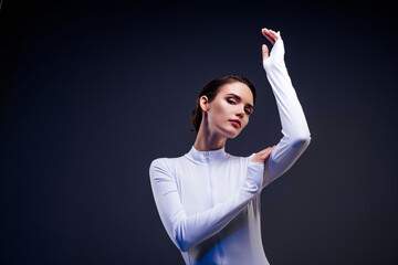 Elegant young woman posing in a white bodysuit against a dark background, showcasing beauty