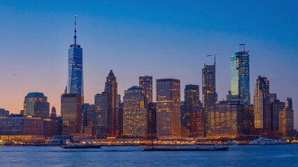 Obraz premium New York City illuminated skyline reflecting sunset light over calm waters