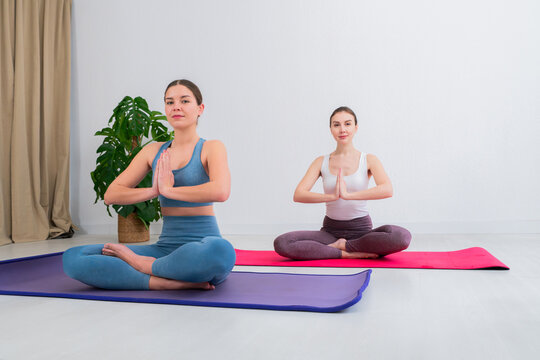 Two young women practicing yoga together in a serene space while performing various meditation poses on mats with a sense of tranquility and calmness in their focused expressions and movements