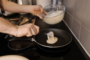 A close-up shot of a man pouring pancake batter mix into a hot frying pan, soft focus.