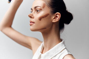 Elegant young woman applying makeup with brown tones, showcasing natural beauty and confidence in a minimalist setting.
