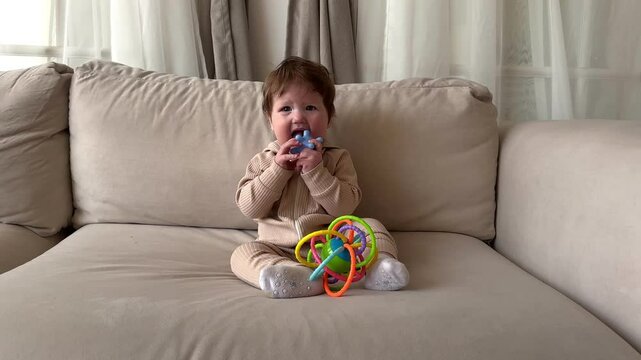 beautiful baby on the couch playing with a toy. chewing teether, concept teething, first teeth, gums, toddler