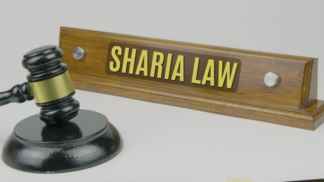 "Sharia Law" text on a wooden nameplate with a gavel tapping once and three times on a white background, symbolizing the Islamic legal system based on the Quran and Hadith