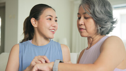 Young adult child give gift AI smart watch IOT app to mature middle age old mum. Love health care older mom asia elder people sit at home sofa happy family wear wrist trace help protect aging life.