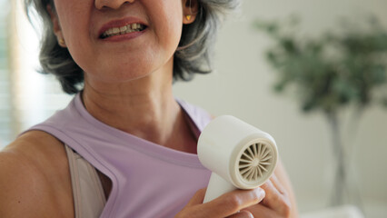 Asia adult people middle age old woman sit at sofa home feel hot flash fever use fan waving hand...