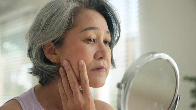 Asia adult people middle age old woman look at mirror dry skin face hand touch neck cheek stress sad at home elder health care aging beauty issue. Asian female aged eye botox filler plastic surgery.