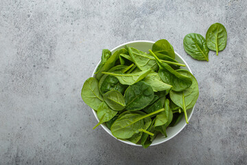 Fresh spinach leaves in a white bowl set on a gray backdrop, showcasing their vibrant green color...