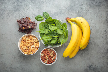Assorted magnesium rich foods like bananas, spinach, peanuts, cashews, and dark chocolate on a gray...
