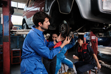 Professional workers teams, multiracial engineers, and mechanics coworkers cooperate to fix and maintain car suspensions together in garage station, and service jobs in automotive transport industry.