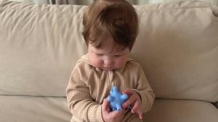 beautiful baby on the couch playing with a toy. chewing teether, concept teething, first teeth, gums, toddler