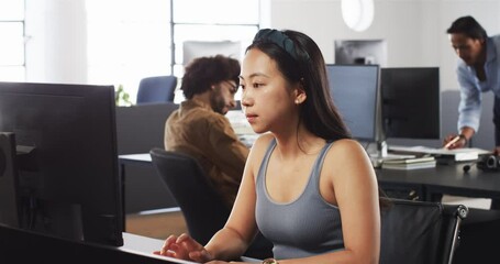 Happy male colleagues working and helping chinese female colleague working on computer in office