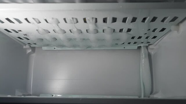 Freezing water gradually transforming into perfectly shaped ice cubes within refrigerator's automatic ice maker, showcasing cold temperature and ice production process