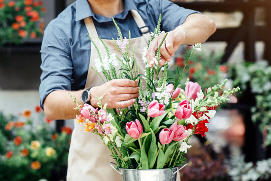 Florist make fresh flowers bouquet arrangement. Busy young male owner in apron and protective mask makes fashionable composition for client at online order in shop with decorative plants, empty space