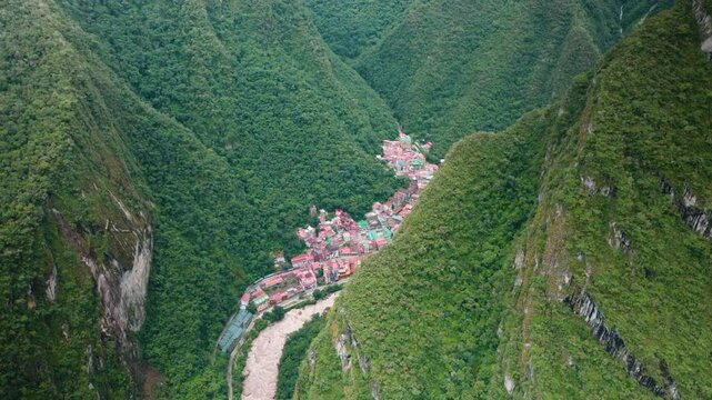 Aerial view of Aguas Calientes, the gateway town to Machu Picchu, nestled in a lush green valley surrounded by mountains and jungle in Peru. Scenic and remote travel destination.

