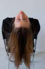 Artistic portrait of a young woman bending backwards over a chair, eyes closed, hair cascading...