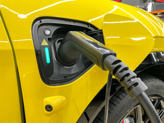 Charging an yellow electric car with a connected power cable close-up.  The concept of ecological...