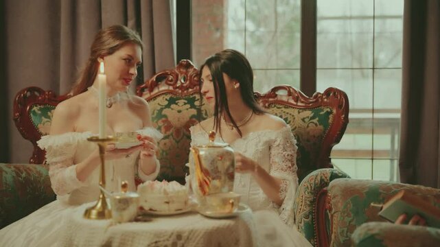 Happy group of women drinking hot tea holding cups in hands golden set. Woman noble lady joy face. retro sofa coffee table. girl rest have tea fun party royal cozy room white vintage dress old style