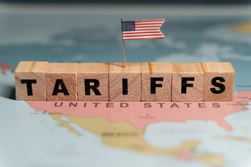  Wooden blocks spelling the word TARIFFS with a small US flag placed on a map of the United States.
