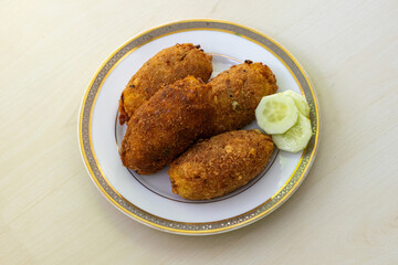 Delicious homemade dim chop on a white plate against a light wooden background. This popular and beloved Bangladeshi snack, also known as dimer chop or dimer alur chop, is a real treat.