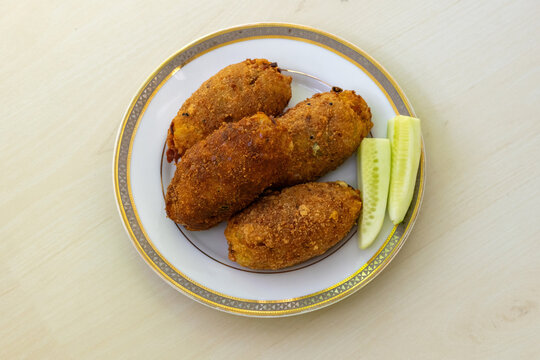 Delicious homemade dim chop on a white plate against a light wooden background. This popular Bangladeshi snack, also known as dimer chop or dimer alur chop, is a true delight. Top view.