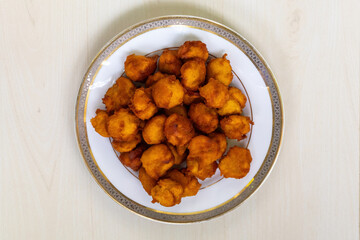 Top view of traditional Bengali taler pitha or taler bora, cakes or pastries made with tal palm fruit pulp, served on a white plate on a light wooden surface.