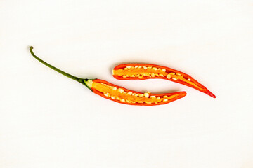 A fresh red chili, cut in half to reveal its inner texture and seeds, is isolated on a white...
