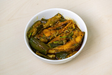 Delicious brinjal curry cooked with hilsa fish (Tenualosa ilisha), served in a white bowl on a light wooden surface.