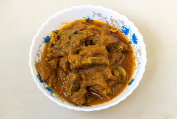 Delicious mutton curry in a white bowl on a light wooden table background. Mutton bhuna is a very tasty and spicy dish, popular in Bengali (Bangladesh) cuisine.
