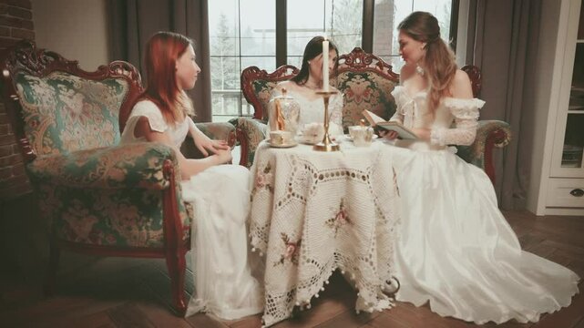 Happy group of women in living room and discussed novel book. Woman noble lady joy face retro sofa coffee table. girl rest have tea fun party royal cozy room white vintage dress old victorian style