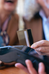 Unrecognizable senior couple at an outdoor cafe making a card payment. Both wearing trendy outfits and sunglasses. Ideal for retirement, finance, lifestyle, and senior couple relationship concepts. 