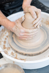 Close-up of a potter's hands working on a pottery wheel. Vertical photo. 