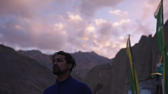 4K footage of an individual lost in thought while gazing at a vibrant sunset over mountain landscapes.