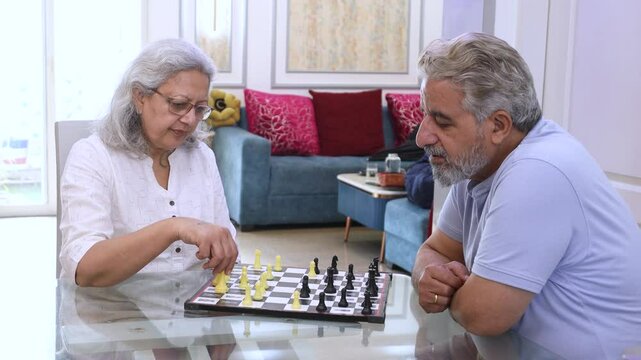 Happy retired senior indian couple playing game of chess and engaging in a friendly competition. hobby and fun activity, Retirement .life. Asian husband wife enjoy Indoor sport. 4k - Powered by Adobe