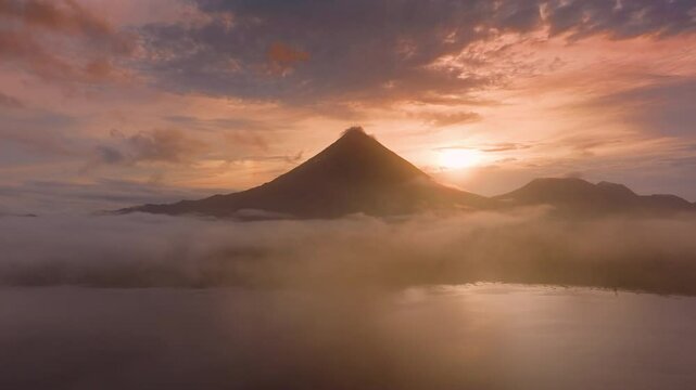 Experience stunning aerial views of the sunrise over Laguna de Arenal and Volcan Arenal in Costa Rica, surrounded by mist and greenery, creating a tranquil paradise for nature lovers