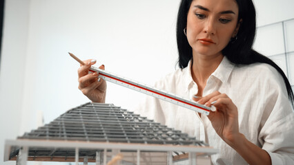 Professional young beautiful architect engineer using ruler and pencil measuring model roof length...