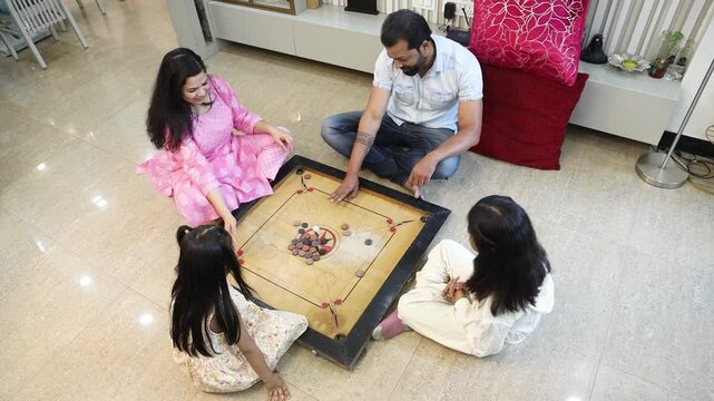 Indian family playing carrom board game at home. Parents having fun time with kids enjoy indoor sport in summer. Playful children. Hobby and fun. Togetherness and bonding.