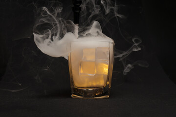 Opaque transparent ice filled drink short glass yellow tungsten light flame smoke fog on black...