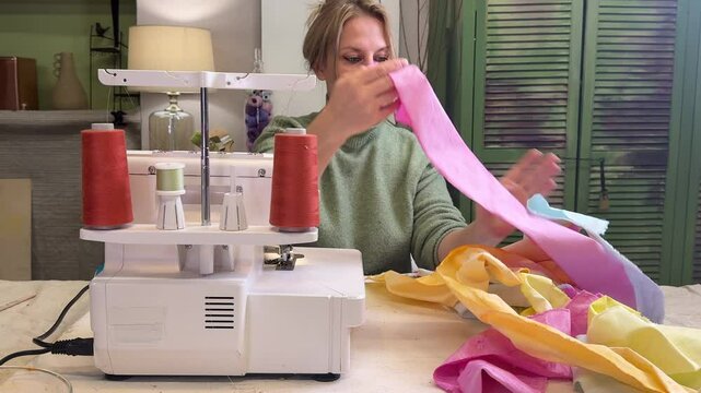 a woman sits behind an overlock in a home sewing room and is about to sew