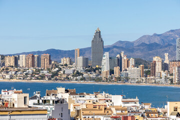 Aerial drone photo over looking the old town of Benidorm in Spain showing apartments and high rise buildings on the Poniente Beach front with the ocean and mountains in the background on a sunny day