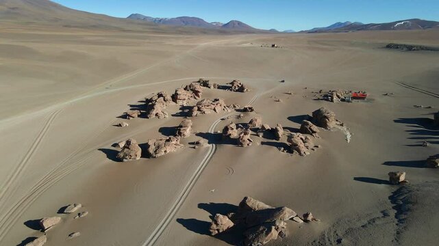 Aerial tracking over sandy road cutting across Siloli desert with hills rising around path