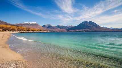 A scenic view of a beach with clear turquoise water and mountains in the background under a blue sky