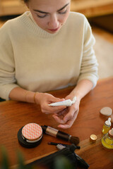 woman applying a makeup primer to her face in front of a mirror. The makeup products are neatly...